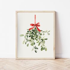 an art print with watercolor leaves and red ribbon hanging on a wall in a room