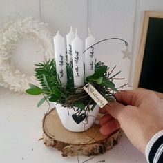 a hand holding a small white candle holder with six candles in it and greenery