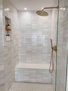 a walk in shower sitting next to a white tiled wall with shelves on the side