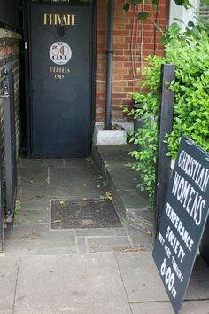 an entrance to a restaurant with signs on the sidewalk and bushes in front of it