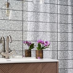 two vases filled with flowers sitting on top of a bathroom counter next to a sink