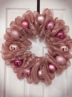 a wreath with pink ornaments hanging on the front door