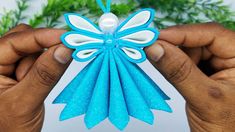 two hands holding an ornament in the shape of a blue and white butterfly