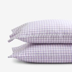 two pillows sitting next to each other on top of a white surface with purple checkered sheets