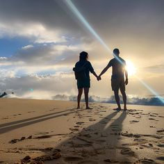 two people holding hands while standing on top of a sand dune at sunset with the sun behind them