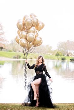 a woman in a black dress is holding some gold balloons and posing for the camera