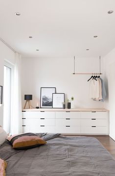 a bed sitting in a bedroom next to a white dresser and window with pictures on it