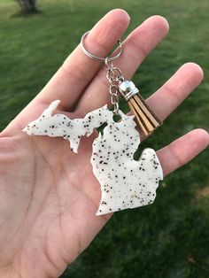 a hand holding a keychain shaped like the state of michigan, with black speckles on it