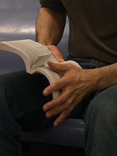 a man sitting down reading a book with his hands resting on the book's cover