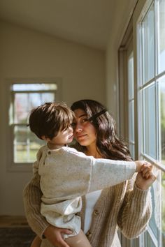 a woman holding a child looking out the window with her arm around another woman's shoulder