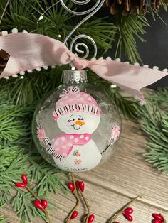 a glass ornament with a snowman on it's face and pink ribbon