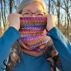 the woman is wearing a multicolored knit cowl with her hands on her face