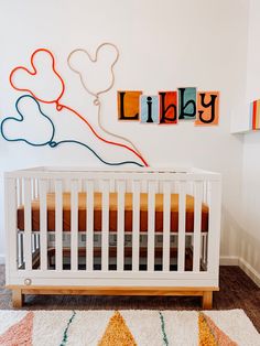 a white crib in a nursery with mickey mouse wall art