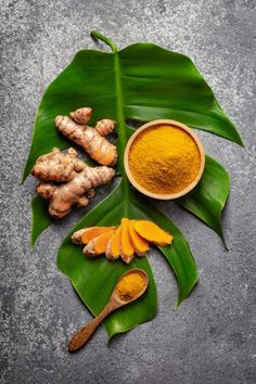 tumerical, ginger and other spices on a leaf with some green leaves around it