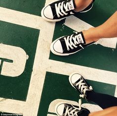 two people wearing black and white tennis shoes standing on a green floor with their feet crossed