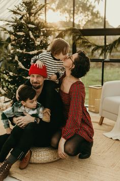 a family is sitting on the floor in front of a christmas tree and kissing each other