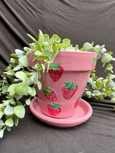 a pink planter with strawberries painted on it next to a potted plant