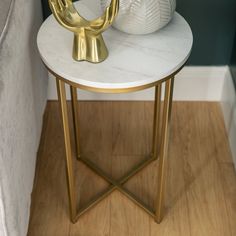 a white and gold side table with a vase on it's top next to a wall