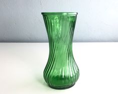 a green glass vase sitting on top of a white table next to a gray wall