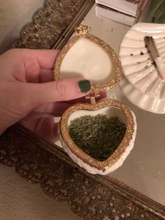 a person holding a small heart shaped box filled with green stuff in front of a mirror