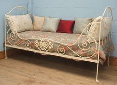 a white metal day bed sitting on top of a hard wood floor next to a blue wall