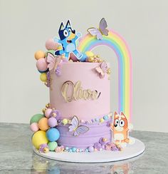 there is a pink cake decorated with cartoon characters on the top and rainbow decorations around it