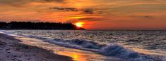 the sun is setting over the water at the beach with waves coming in to shore