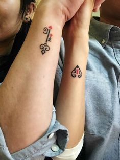 two people with matching tattoos on their arms, one holding the other's arm