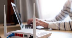 a router sitting on top of a wooden table next to a person using a laptop