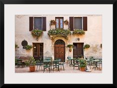 an old building with tables and chairs in front of it, surrounded by potted plants