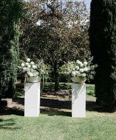 two large white vases with flowers on them sitting in the middle of a park