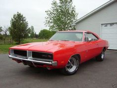 a red muscle car parked in front of a garage