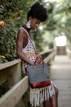 a woman sitting on a wooden bench holding a gray and red bag with tassels