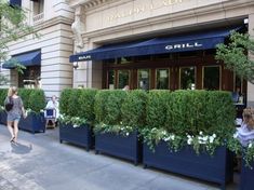 people walking down the sidewalk in front of a restaurant with tall blue planters on either side