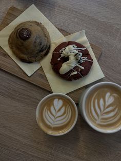 two cups of coffee sit next to an iced cookie