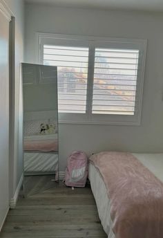 a bedroom with a bed, dresser and mirror in it's corner next to a window