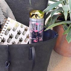 a black bag with pink flamingos and pineapples on it is sitting next to a potted plant