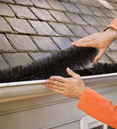 a woman is cleaning the gutter on top of a roof with a black brush