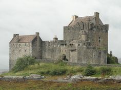 an old castle sitting on top of a lush green hillside next to a body of water