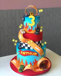 a three tiered birthday cake with cars and stars on the top, sitting on a table