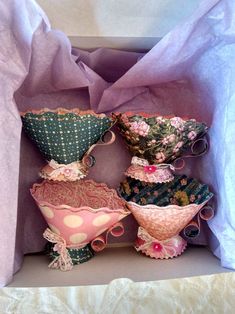 several decorative vases are in a box on the tablecloth covered surface, one is pink and two are green