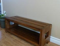 a wooden bench sitting on top of a hard wood floor next to a white wall