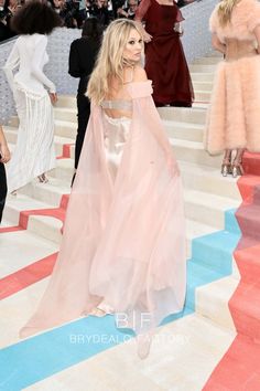 a woman in a long pink dress walking down the stairs with other people behind her