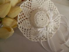 a crocheted doily hat next to yellow tulips on a table