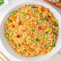 a white bowl filled with rice and veggies next to some chopsticks