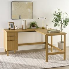 a wooden desk sitting on top of a rug next to a plant in a vase