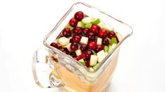 a glass mug filled with apples and cranberries on top of a white table