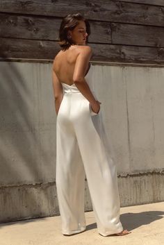 a woman standing on the sidewalk wearing white pants and a halter top with her back to the camera