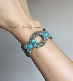 a woman's arm wearing a bracelet with turquoise beads and bead work on it