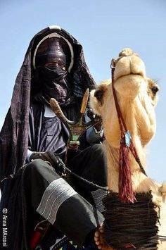 a man riding on the back of a camel wearing a black outfit and head covering